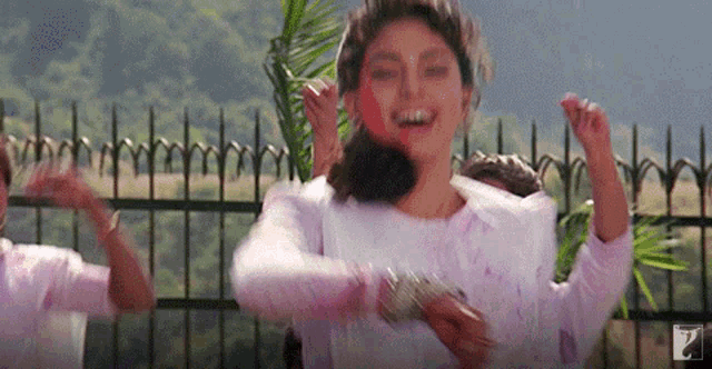 a woman in a white shirt is dancing in front of a fence with the number 7 on the bottom