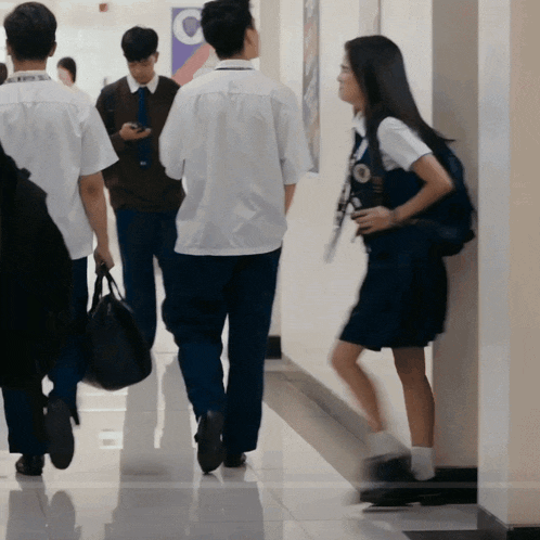 a group of people walking down a hallway with a c on the wall behind them