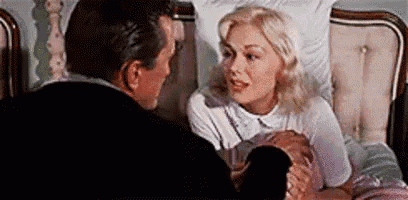 a man and a woman are sitting in a bed talking to each other . the woman is holding a baby .
