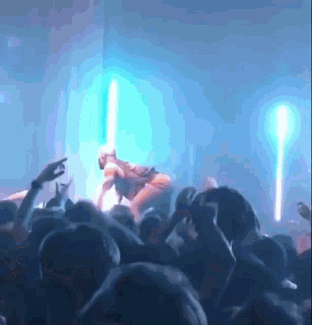 a crowd of people are watching a performer on stage with a blue light behind them