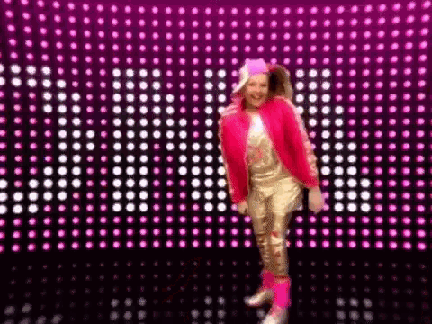 a girl in a pink jacket and hat is dancing in front of a wall of lights .