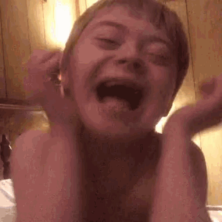 a young boy is making a funny face with his mouth open and his hands up .