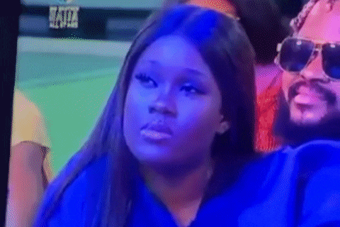a woman wearing sunglasses and a blue shirt is sitting next to a man with a beard on a television screen .