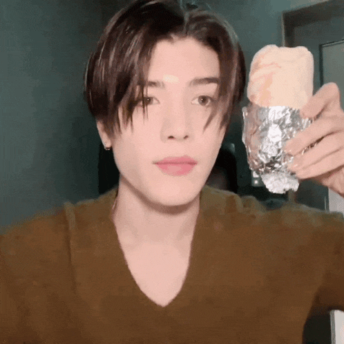 a young man is holding a burrito wrapped in tin foil in his hand .