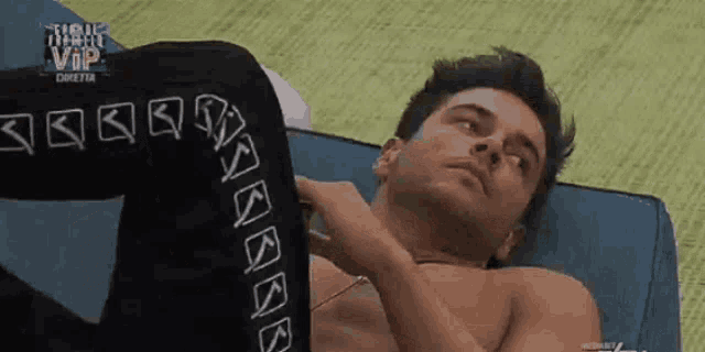 a shirtless man is laying on a blue couch and looking at the camera .