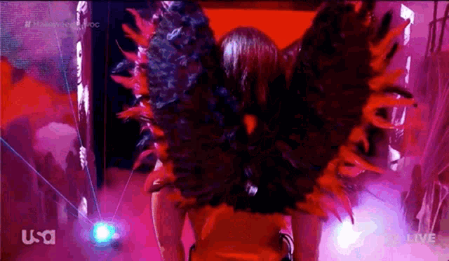 a woman in a red dress with feathered wings is on a usa live broadcast