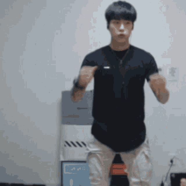 a young man in a black shirt and khaki pants is standing in front of a white wall .