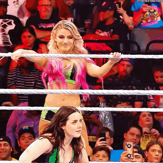 a woman with pink hair is standing in a wrestling ring while another woman looks on