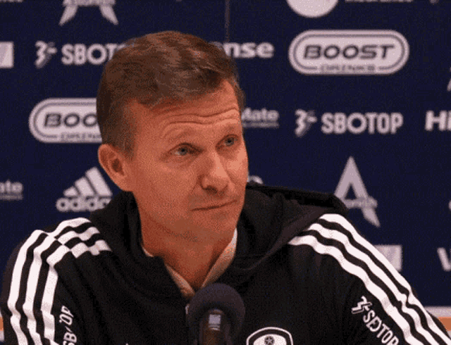a man wearing a black and white adidas jacket is sitting in front of a boost sign