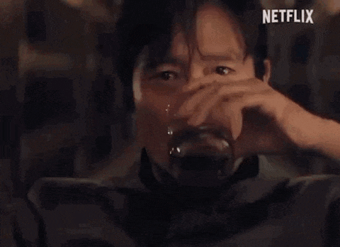 a man is holding a glass of whiskey and making a funny face .
