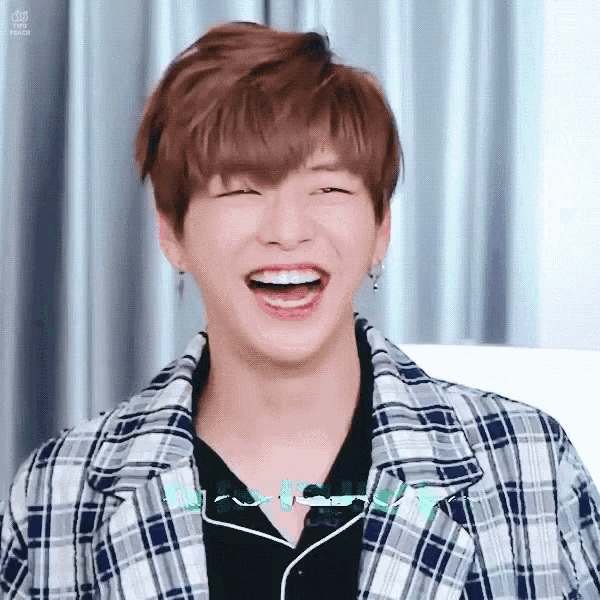 a young man in a plaid jacket is laughing with his mouth open .