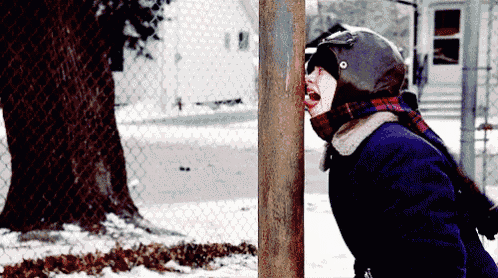a person wearing a helmet and scarf is sticking their head through a chain link fence in the snow .