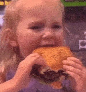 a little girl is eating a large hamburger with her mouth open