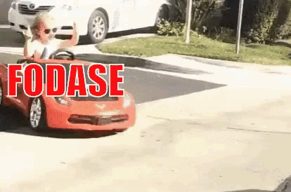 a child is driving a red toy car on the street .