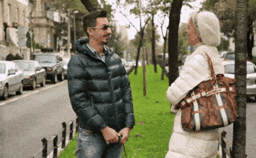 a woman with a louis vuitton purse talks to a man on the sidewalk
