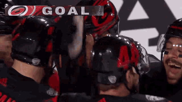 a group of hockey players celebrate a goal with a scoreboard behind them