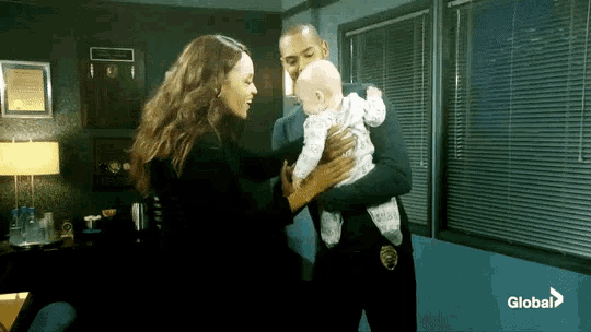 a man in a police uniform holds a baby in his arms while a woman stands behind him
