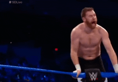 a man without a shirt is kneeling in a wrestling ring with a w logo on the ring .
