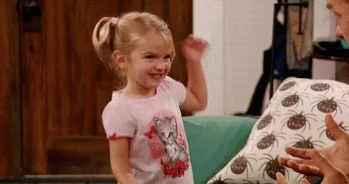 a little girl in a pink shirt with a cat on it is standing next to a pillow with pineapples on it .