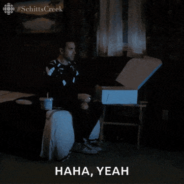 a man sitting on a bed with a box in front of him that says " haha yeah " on it