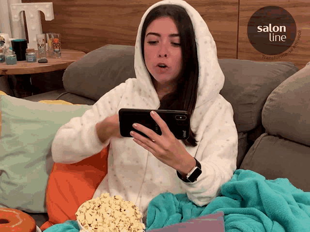 a woman is sitting on a couch looking at her phone with a salon line logo in the background