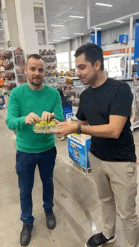 a man in a green sweater is standing next to a man in a black shirt holding a bowl of grapes ..