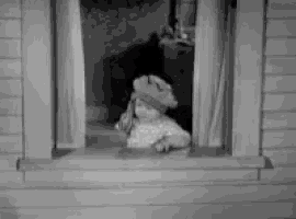 a black and white photo of a baby wearing a hat looking out of a window