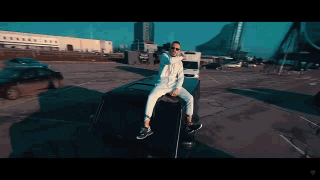 a man in sunglasses sits on the roof of a car in a parking lot