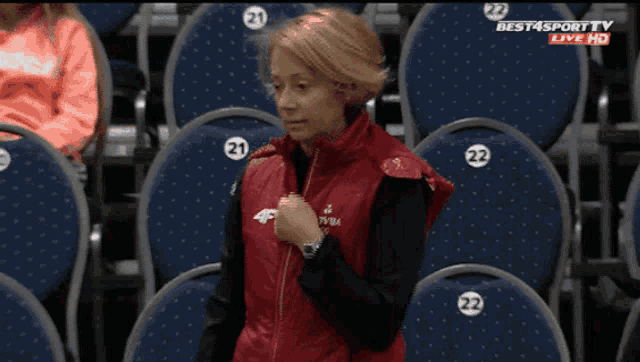 a woman in a red vest is sitting in a stadium watching a game on best4sport tv live