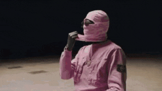a man wearing a pink ski mask and a pink jacket is sitting on the ground .