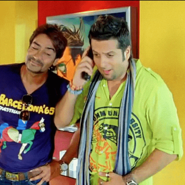 a man wearing a barcelona 65 shirt talks on a cell phone next to another man
