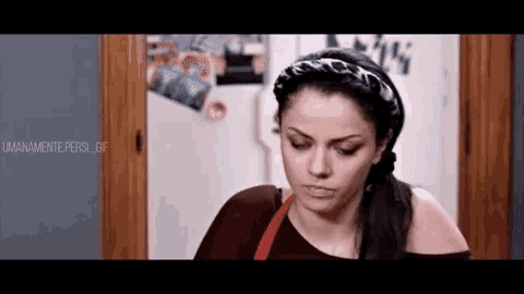 a woman wearing a headband is standing in front of a refrigerator and a door .