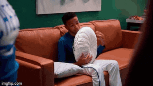 a young man is sitting on a couch holding a pillow .
