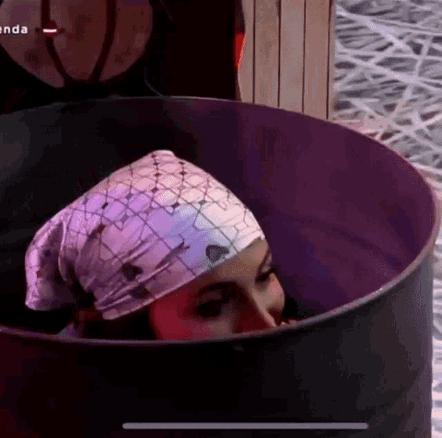a woman wearing a bandana is sitting in a barrel with her head sticking out .