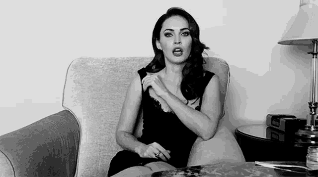 a woman in a black dress is sitting in a chair with her hands on her chest .