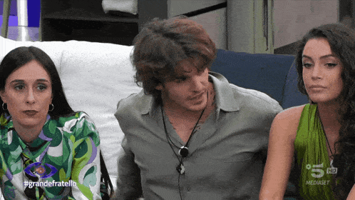 three people sitting on a couch with the words grandefratello on the bottom right