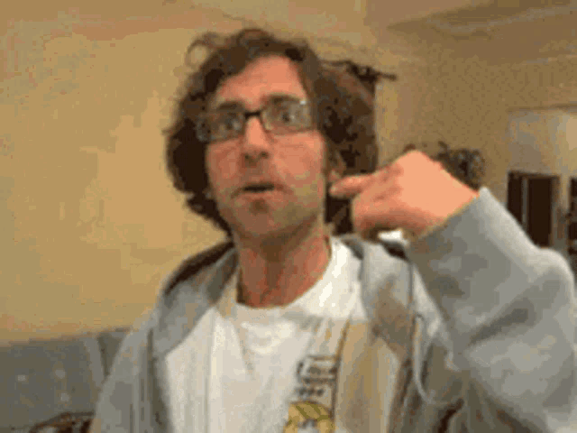 a man wearing glasses and a gray hoodie is pointing at something