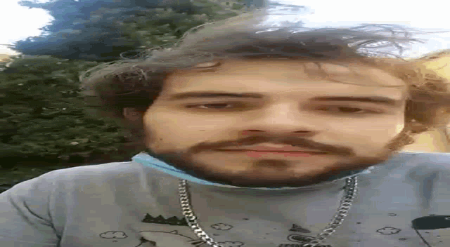 a man with a beard and a chain around his neck is looking at the camera .