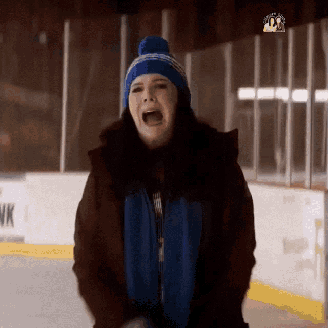a woman wearing a blue hat and a blue vest stands on a ice rink