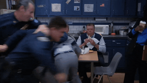 a man sitting at a table eating a sandwich is surrounded by police officers