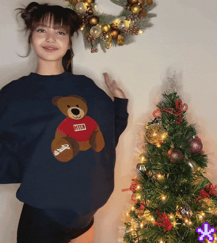 a woman wearing a blue sweater with a teddy bear on it and the word kith on it