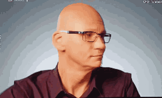 a bald man wearing glasses and a purple shirt looks at the camera