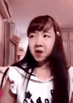a young girl with long hair is making a funny face while wearing a white shirt .