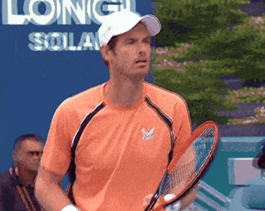 a man in an orange shirt is holding a tennis racquet in front of a sign that says long island