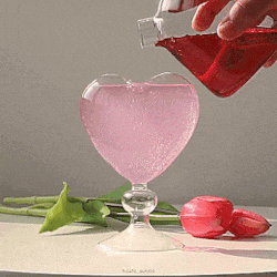 a heart shaped glass is being poured with a red liquid