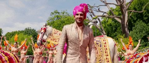a man in a pink turban is standing in front of a parade of people on horses