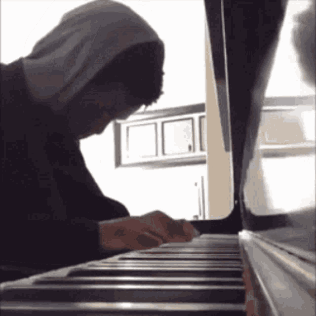 a man is playing a piano with a hoodie on
