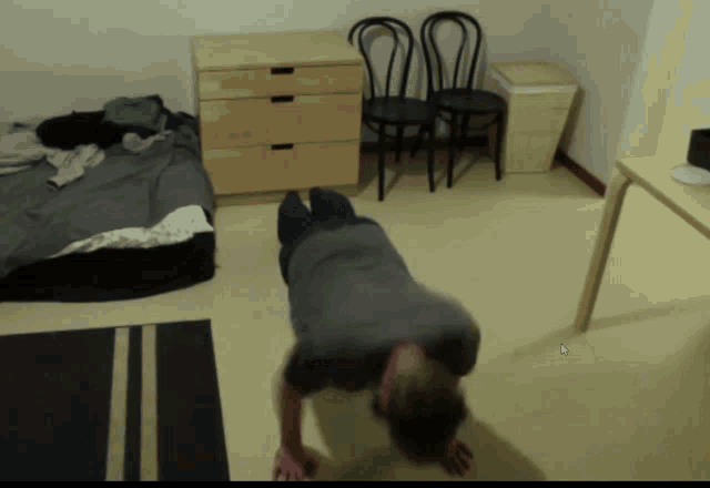 a man is doing push ups in a room with a bed and chairs