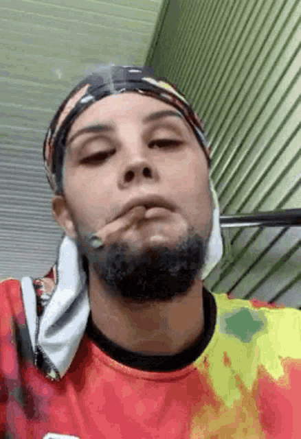a man with a beard is smoking a cigarette while wearing a bandana .