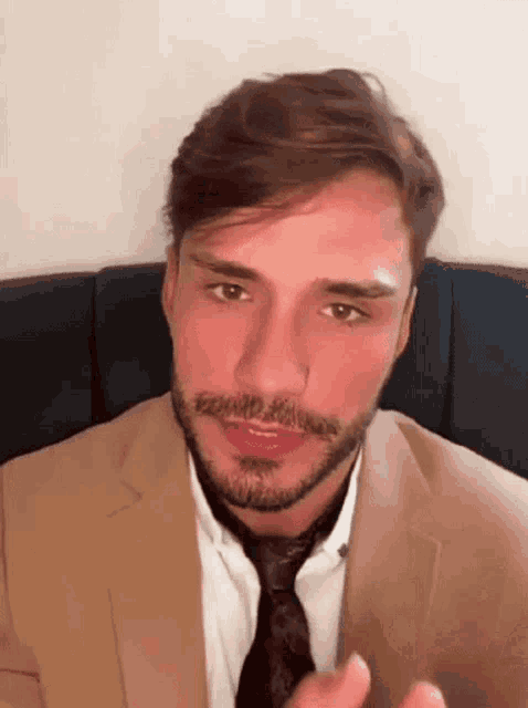 a man with a beard is wearing a suit and tie and sitting on a couch .